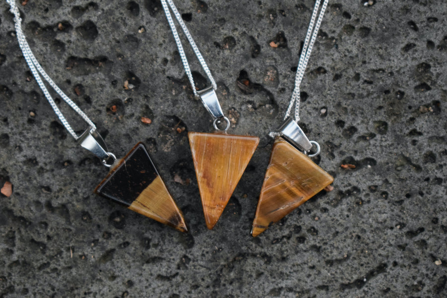 Three tiger's eye triangle pendants on silver chains resting on lava rock