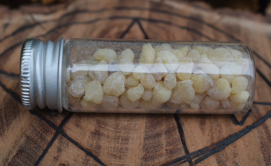 A glass vial filled with frankincense tears or resin resting on a wooden disk with a pentagram pyrography