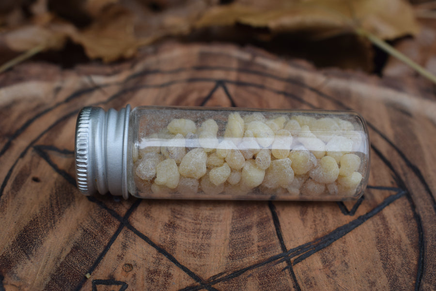 A glass vial filled with frankincense tears or resin resting on a wooden disk with a pentagram pyrography