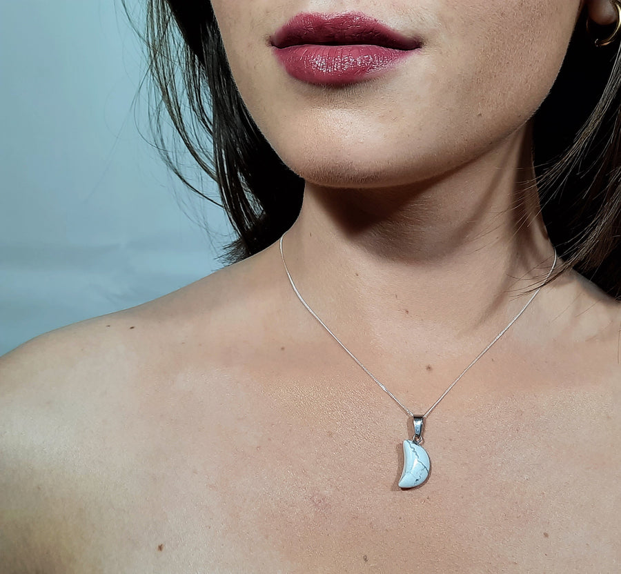 A white howlite crystal crescent moon necklace on a sterling silver chain hanging on the neck of a person