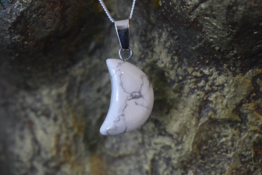 A white howlite crystal crescent moon necklace on a sterling silver chain hanging on the neck of a bronze sculpture