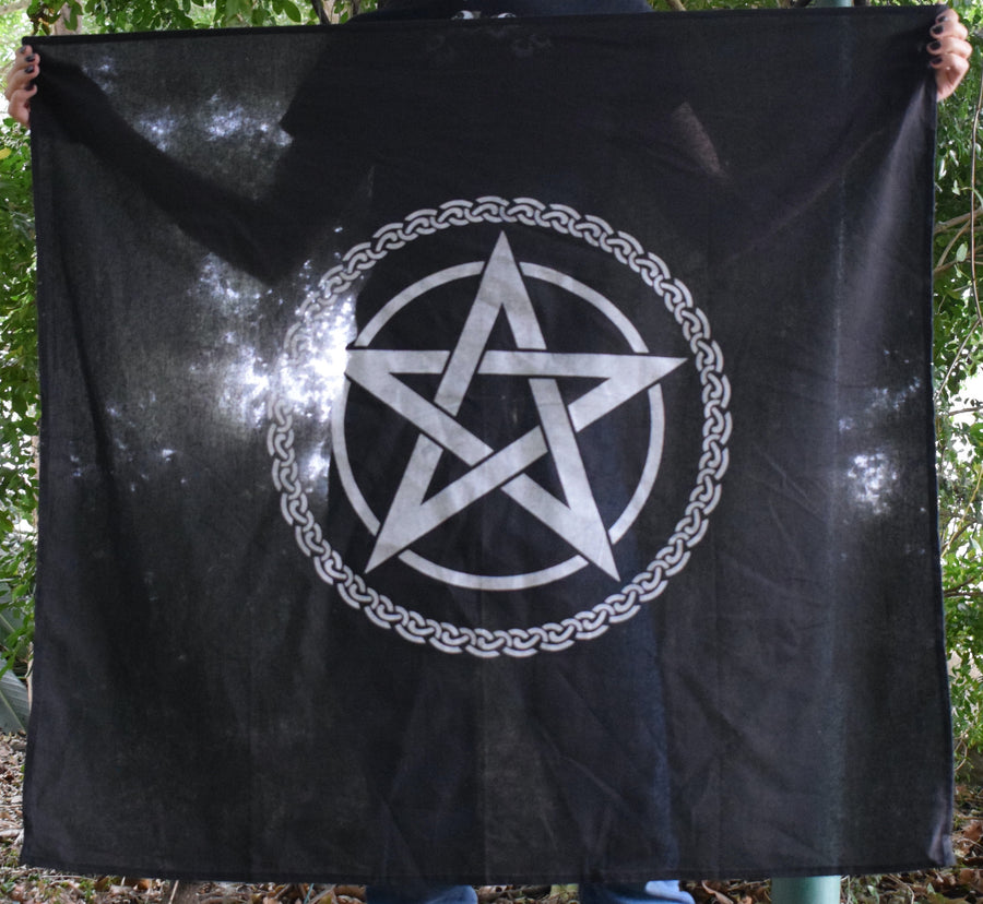 Person holding a large black cotton altar cloth, witches flag tapestry with a tree of life celtic knot circling a white pentagram pentacle