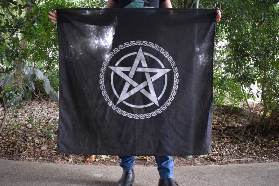 Person holding a large black cotton altar cloth, witches flag tapestry with a tree of life celtic knot circling a white pentagram pentacle
