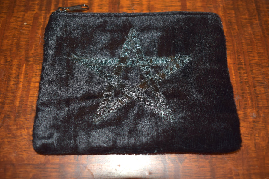 Black velvet zippered purse with pentagram on the front resting on block of timber