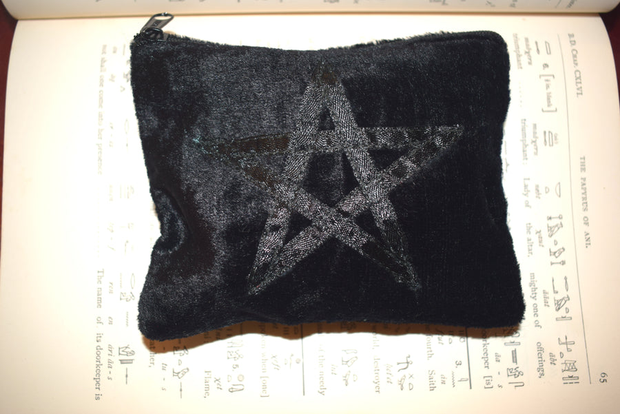 Black velvet zippered purse with pentagram on the front resting on page of Egyptian hieroglyphics 