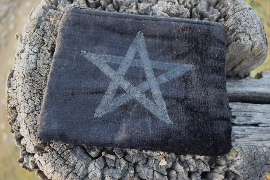 Black velvet zippered bag with pentagram on the front resting on weathered timber paling