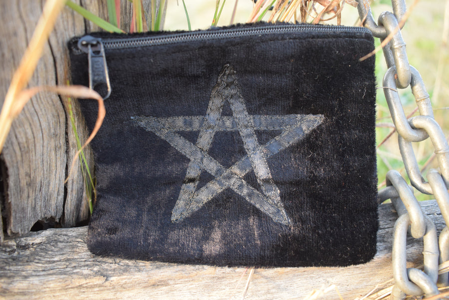 Black velvet zippered bag with pentagram on the front resting on weathered timber paling with old chain