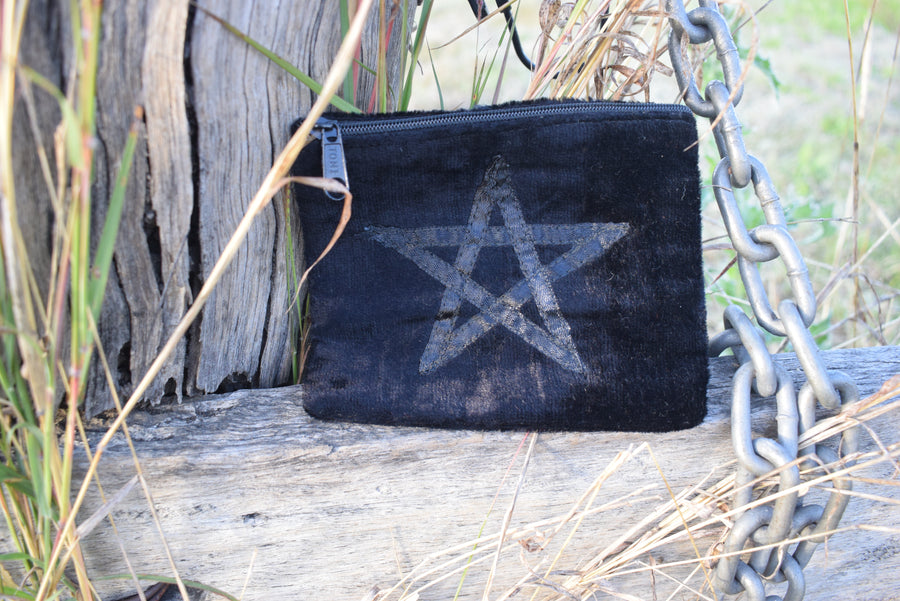 Black velvet zippered bag with pentagram on the front resting on weathered timber paling with old chain