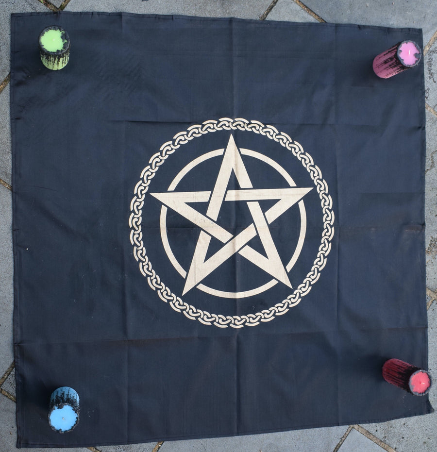 A black satin altar cloth or witches flag with gold pentagram pentacle in the middle encircled by a celtic knot with four coloured candles in each corner