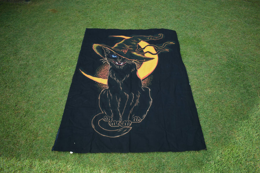 Black hand painted fabric throw depicting a black cat wearing witches hat outlined in yellow and orange with yellow crescent moon in background