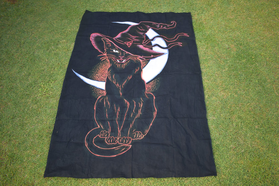 Black hand painted fabric throw depicting a black cat wearing witches hat outlined in pink and orange with white crescent moon in background