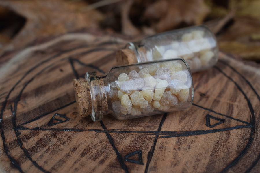 Two glass vials of frankincense tears resting on wood with pentagram pyrography