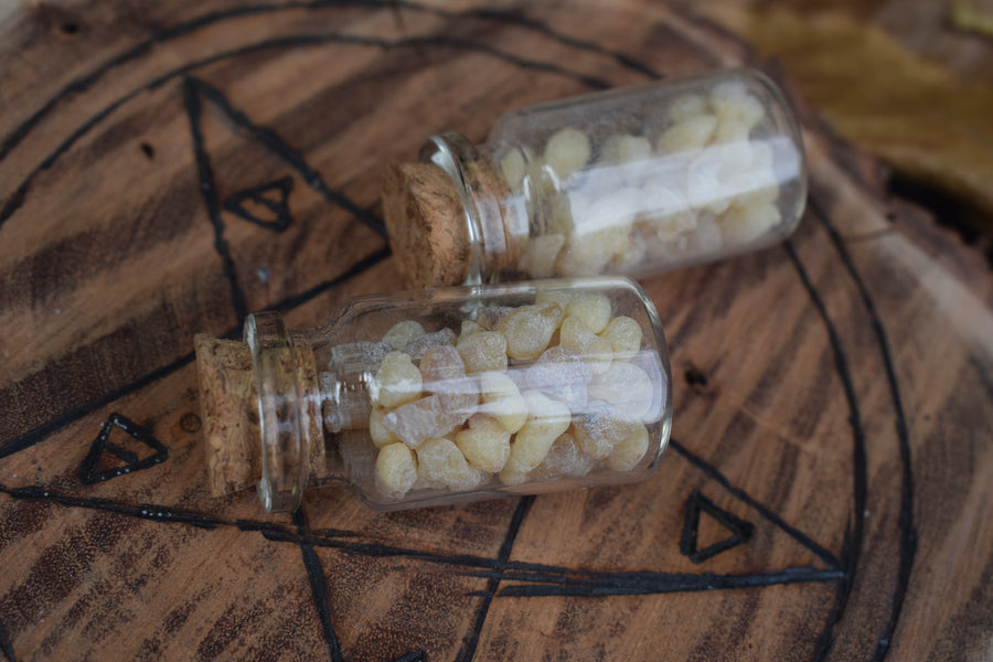 Two glass vials of frankincense tears resting on wood with pentagram pyrography