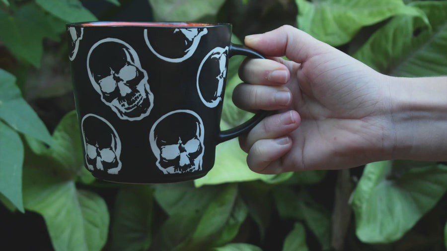 Large black ceramic coffee mug with white skulls and orange inside