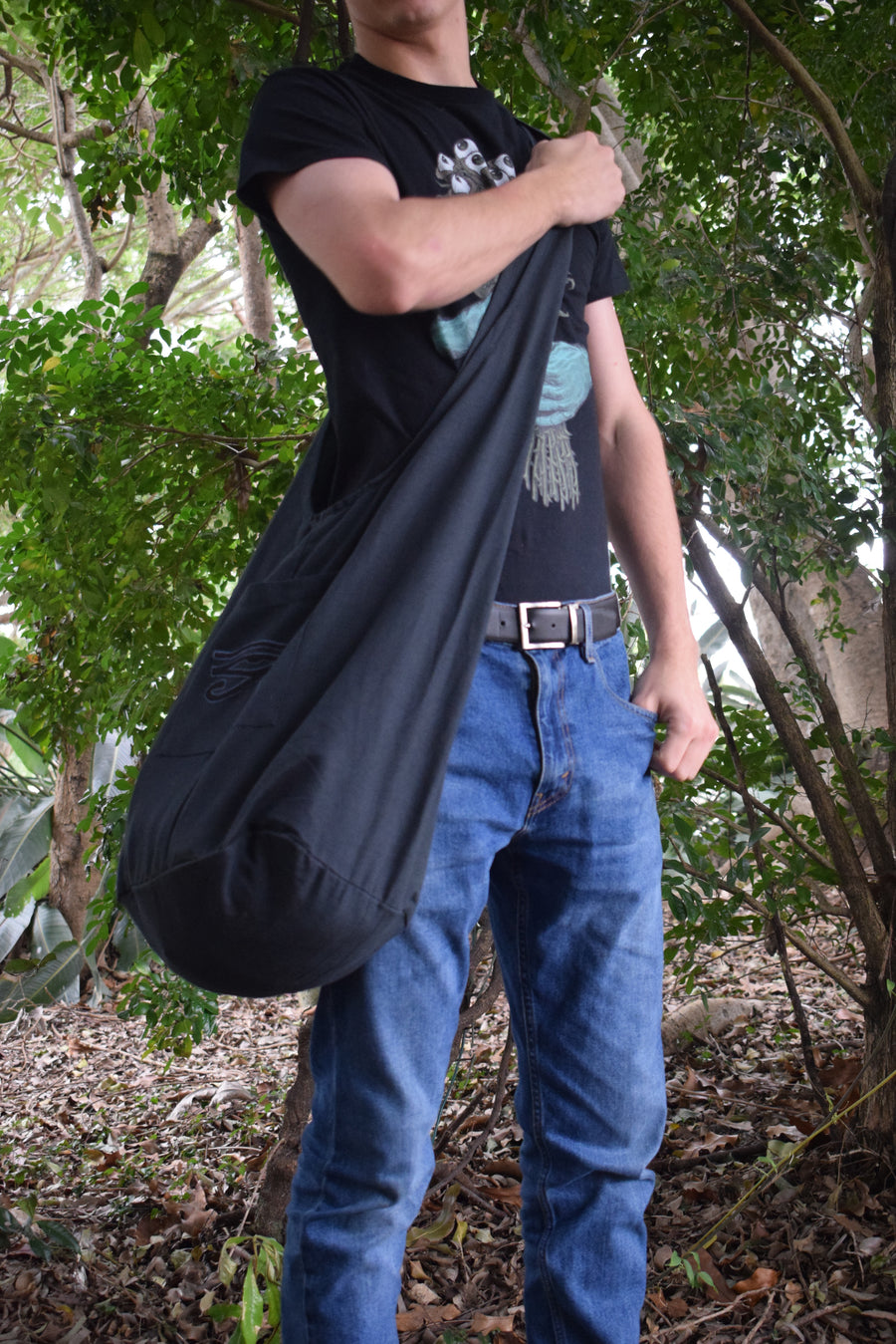 Person standing in forest wearing a black shoulder bag 