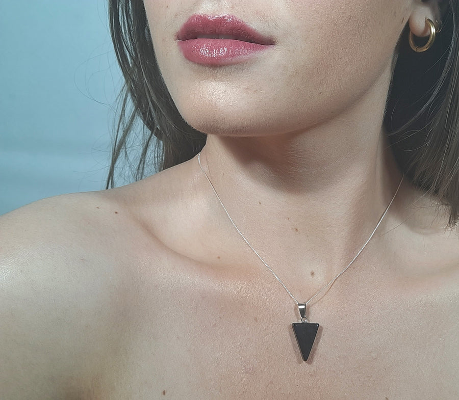 A black tourmaline crystal inverted triangle necklace on a sterling silver chain hanging on the neck of a person