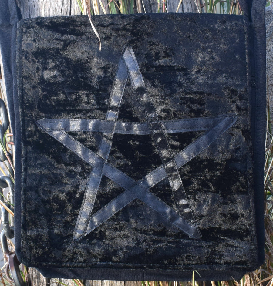 Black velvet bag with a satin ribbon pentagram sewn on the front against weathered timber post and chains