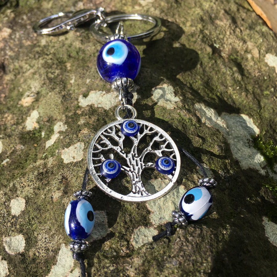 A evil eye tree of life key ring rests on a mossy rock.