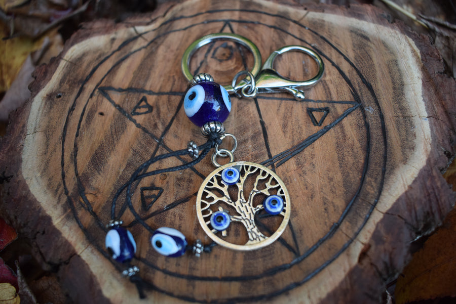 A evil eye tree of life key ring rests on a wooden pentagram disk.