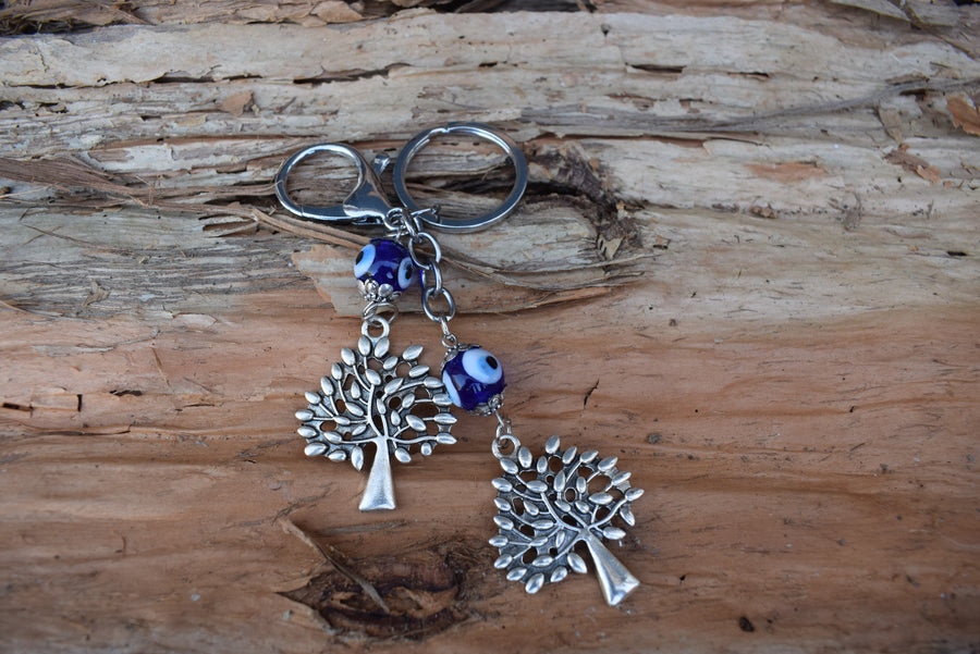 A key ring with two evil eye beads and two silver coloured leafy trees rests on paperbark bark.