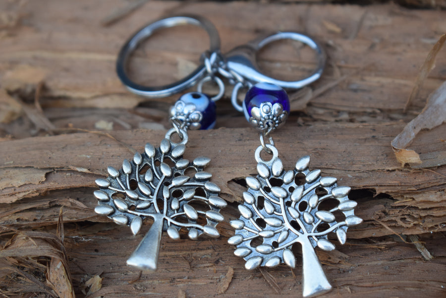 A key ring with two evil eye beads and two silver coloured leafy trees rests on paperbark bark.