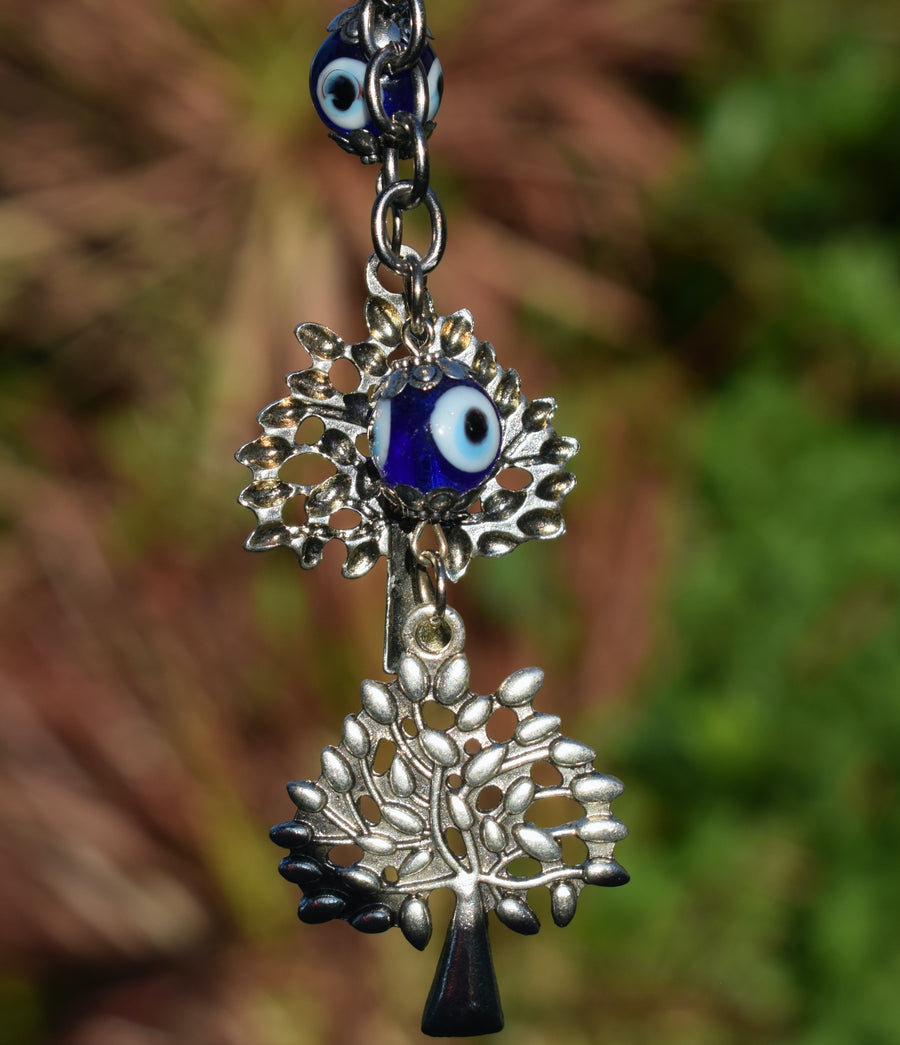 A key ring with two evil eye beads and two silver coloured leafy trees hangs with greenery in the background.