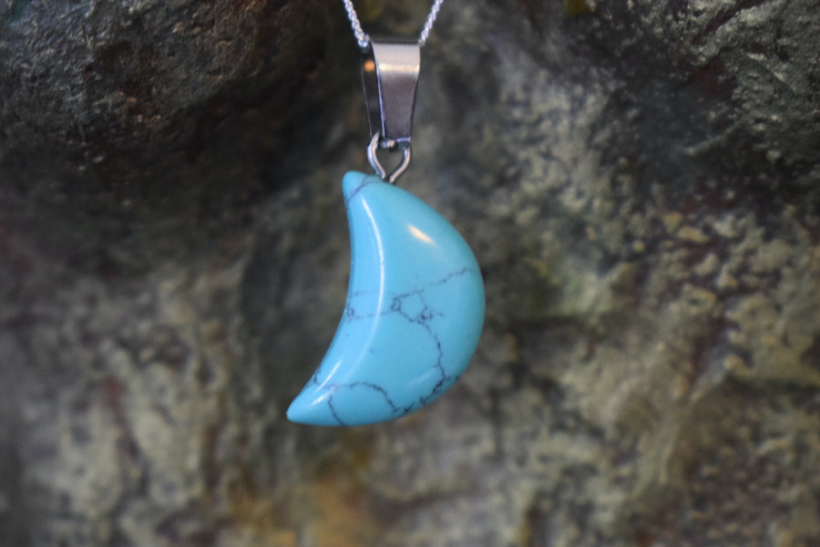 A white howlite crystal crescent moon necklace on a sterling silver chain hanging on the neck of a bronze sculpture