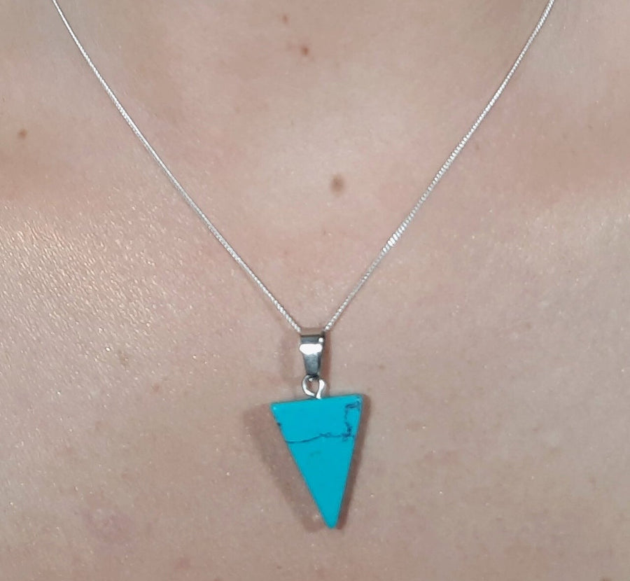 A blue howlite crystal inverted triangle necklace on a sterling silver chain hanging on the neck of a person