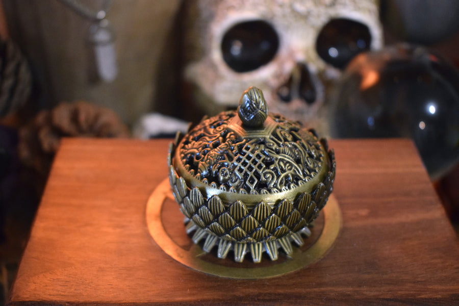 A metal lotus trinket box with a lid resting on a wooden box with a skull in the background
