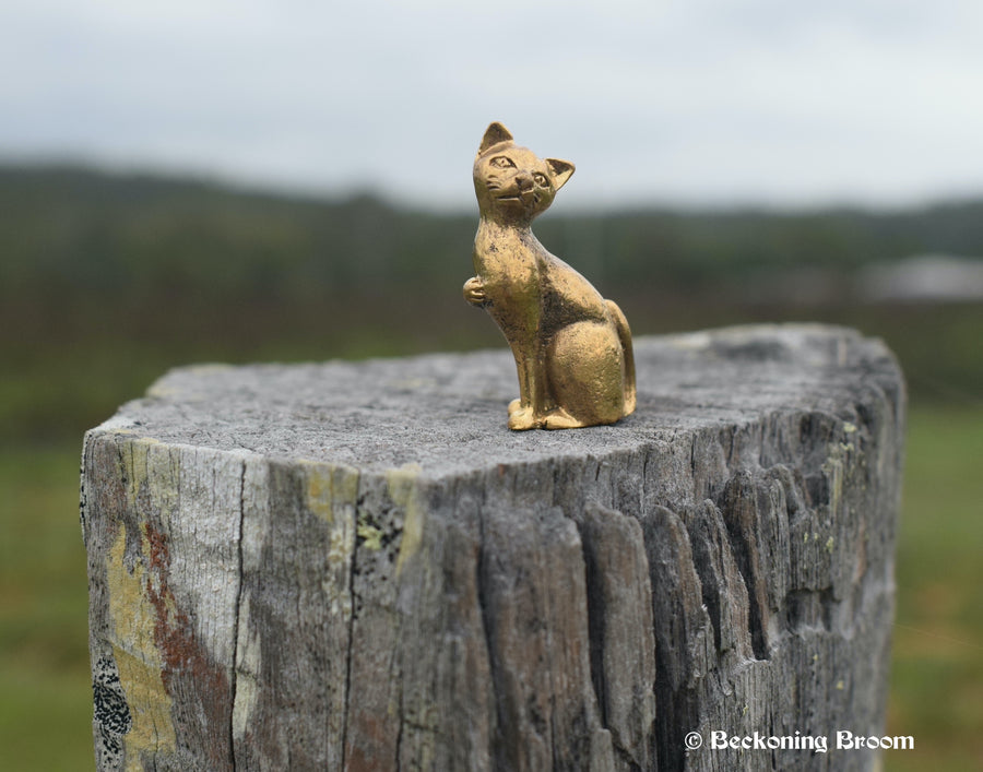 A solid bronze cat figurine sits proudly upon an old stump, looking away from the mountains behind it