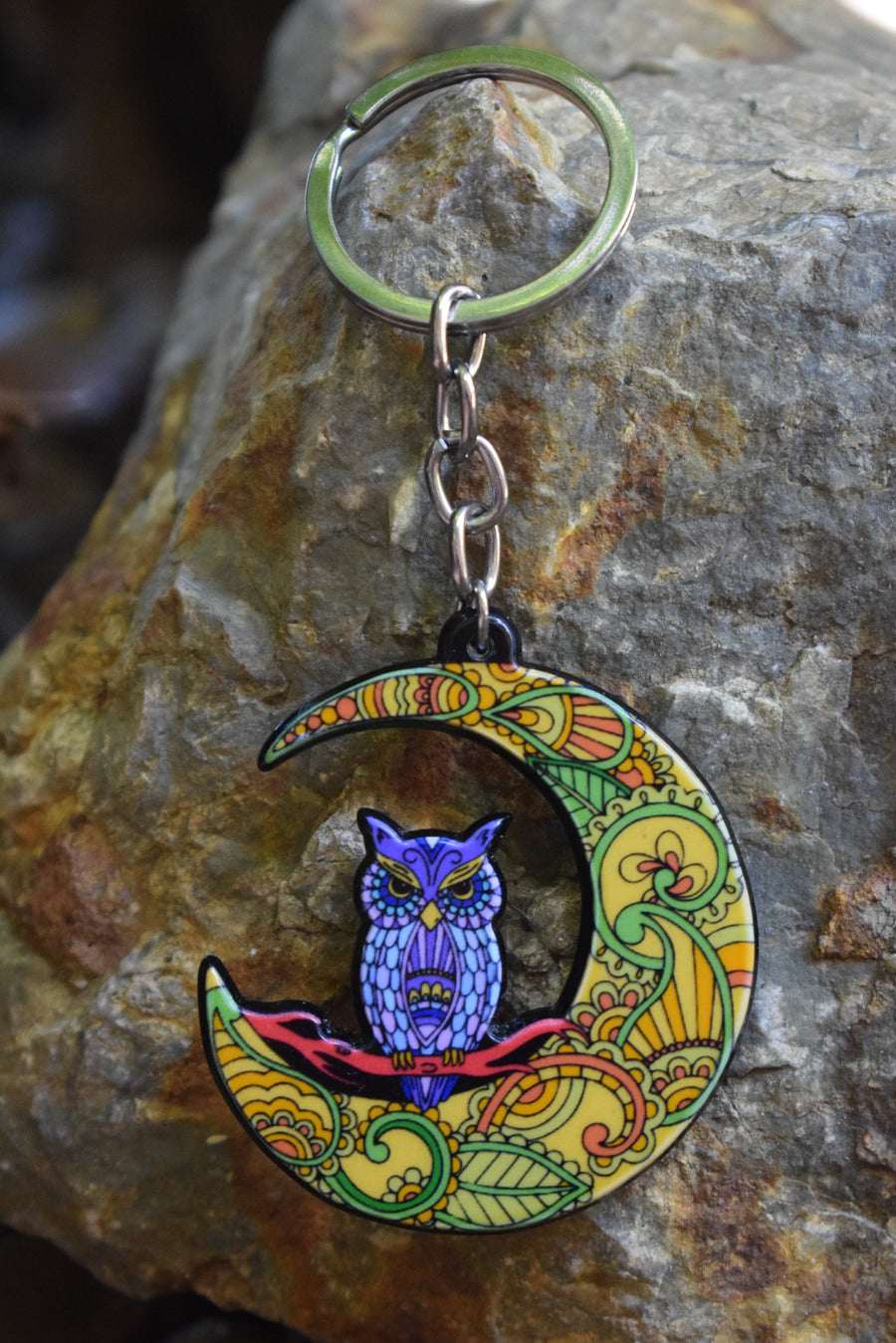 A key ring with a resin blue owl perched on a colourful crescent moon on a rock background.