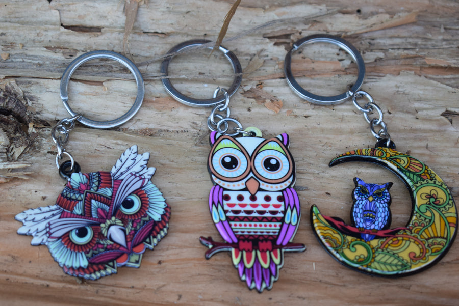 Three different owl key rings resting of a background of paperbark bark.