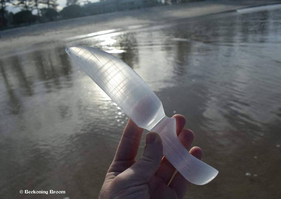A hand holding a selenite dagger with water in the background.