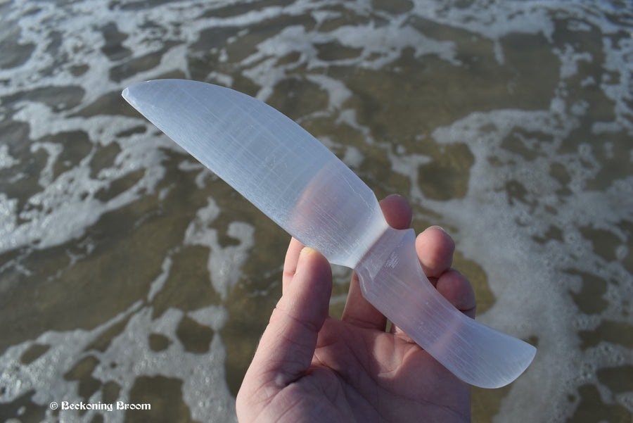 A hand holding a selenite knife with water in the background.