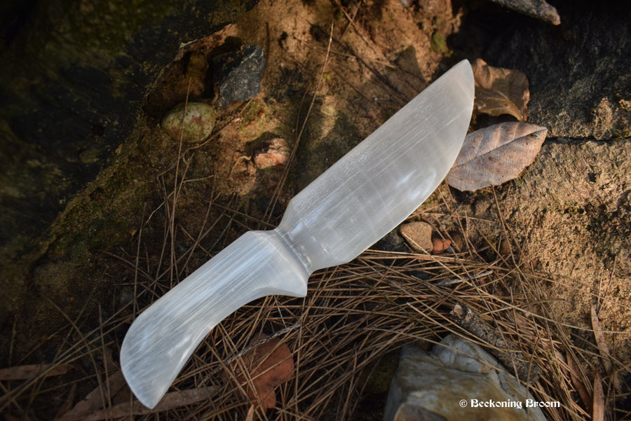 A selenite athame with rocks leaves in the background.