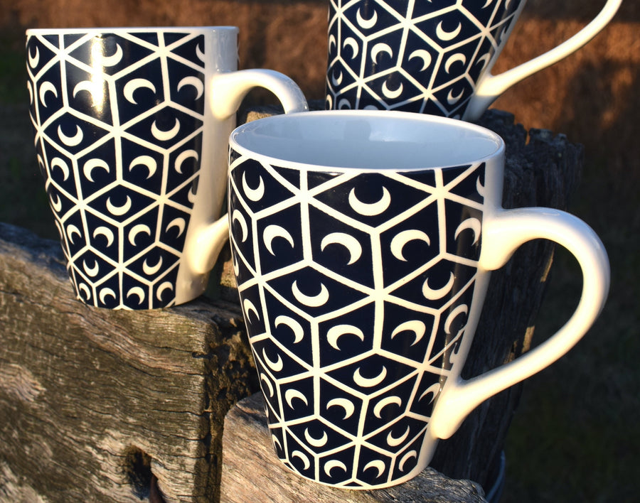 Three black and white cups with crescent moon and sacred geometry design resting on fence palings