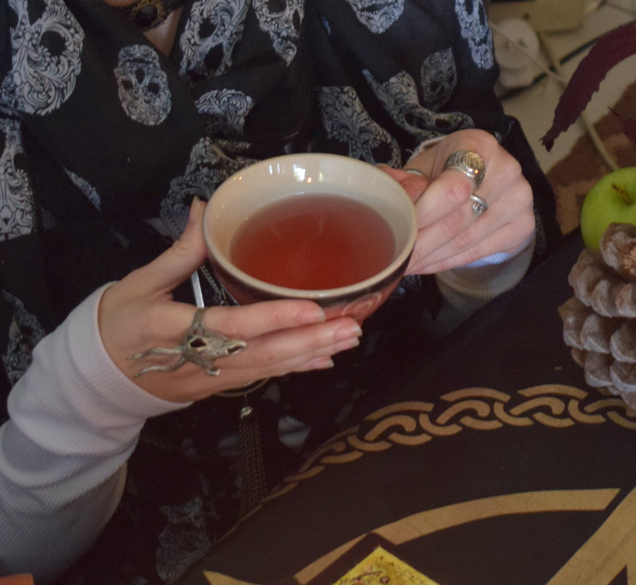 Two hands hold a pink orange tea cup with a triple moon goddess symbol on it