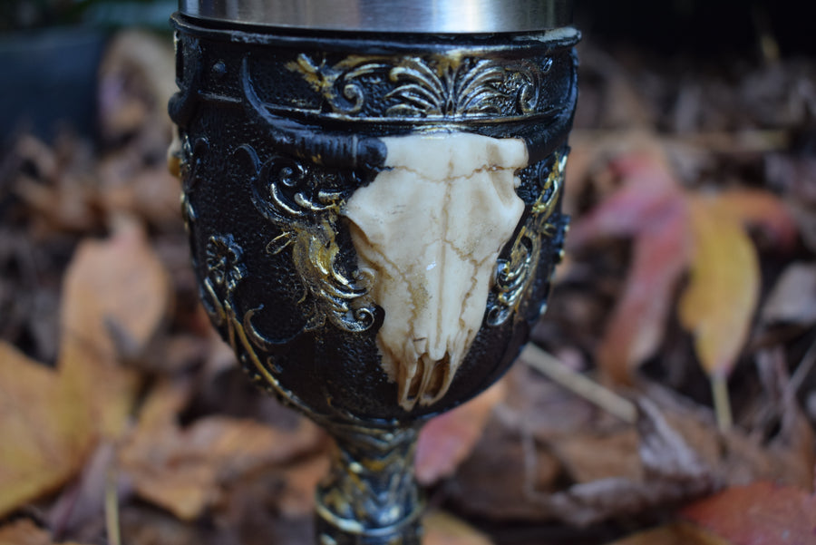 A goblet with a 3d cow skull with horns adorns the outside as it sits on a bed of autumn leaves