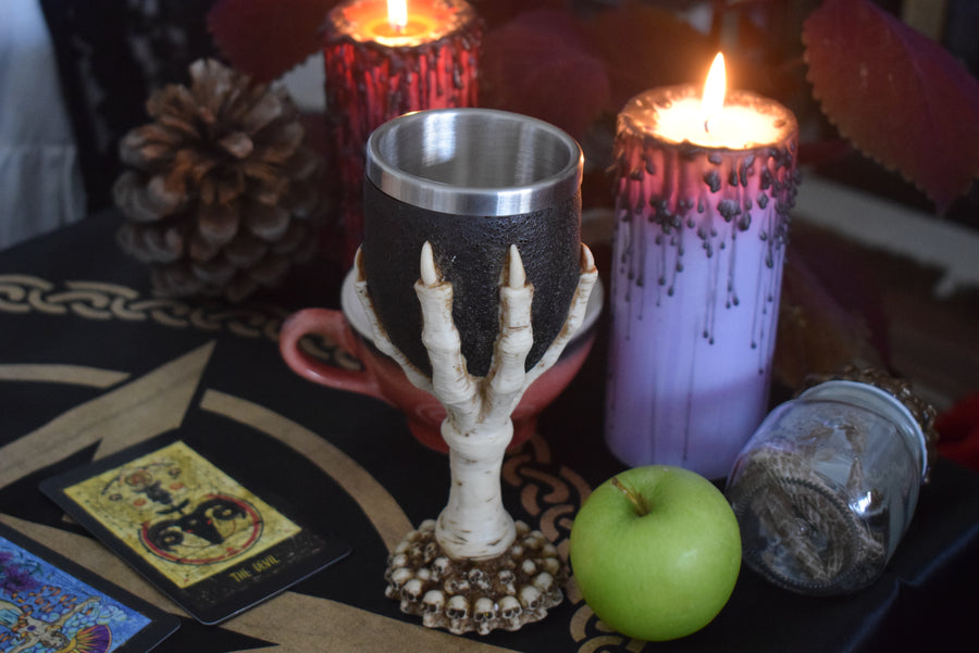 A goblet with a 3d bone dragon claw it rests on an altar with snake skin, candles, and tarot cards
