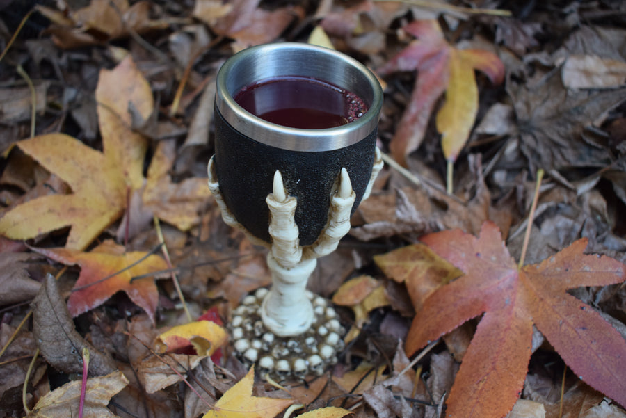 A goblet with a 3d bone dragon claw it sits filled with wine on a bed of autumn leaves