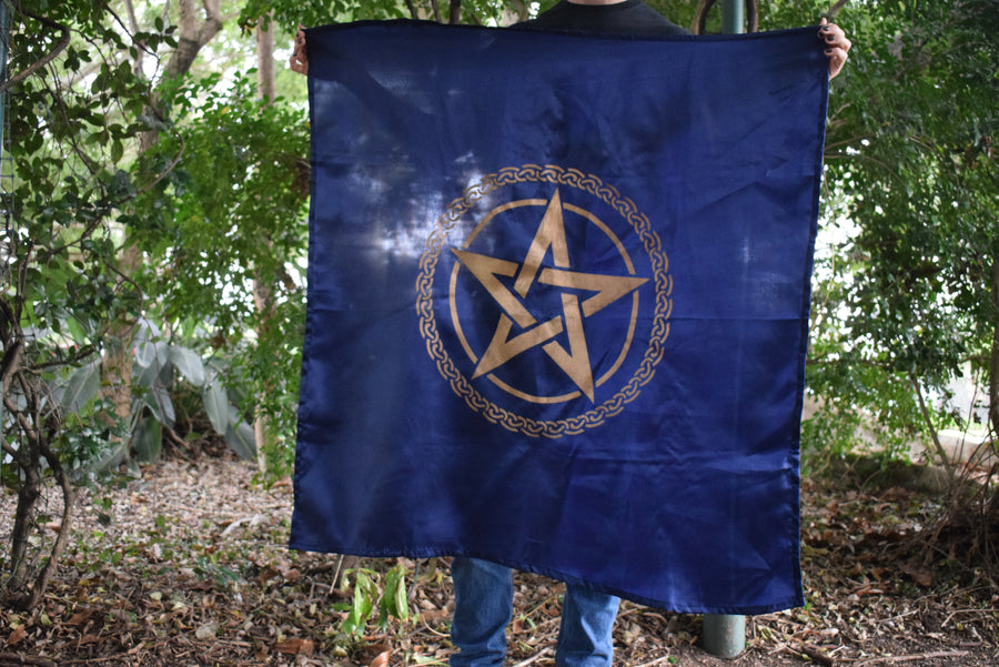 Person holding large royal blue altar cloth, witches flag tapestry with gold tree of life celtic knot encircling a gold pentagram pentacle