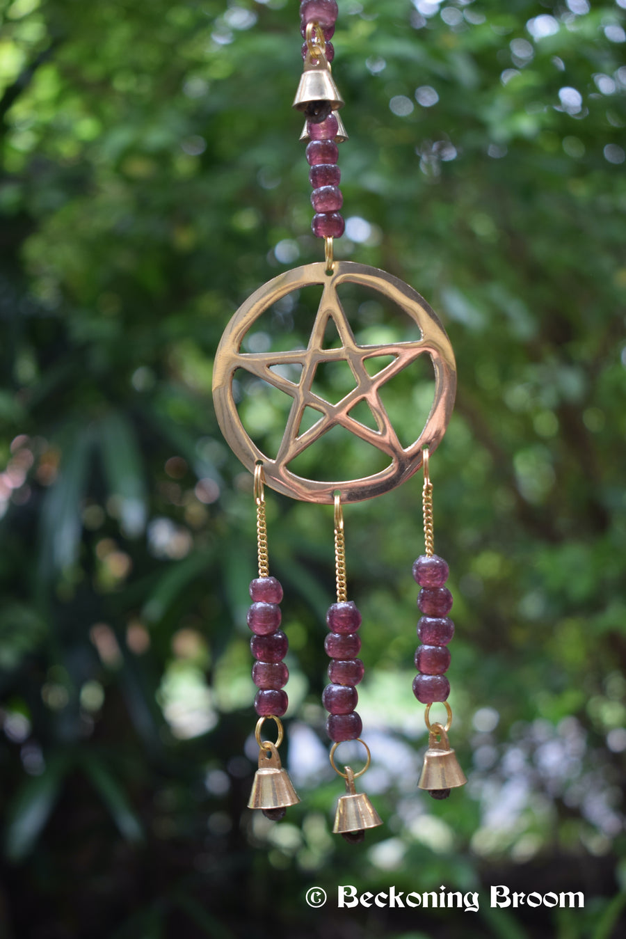 A long bronze metal wind chime with pentagram pentacles, grape purple glass beads and bronze metal bells hanging in the garden.