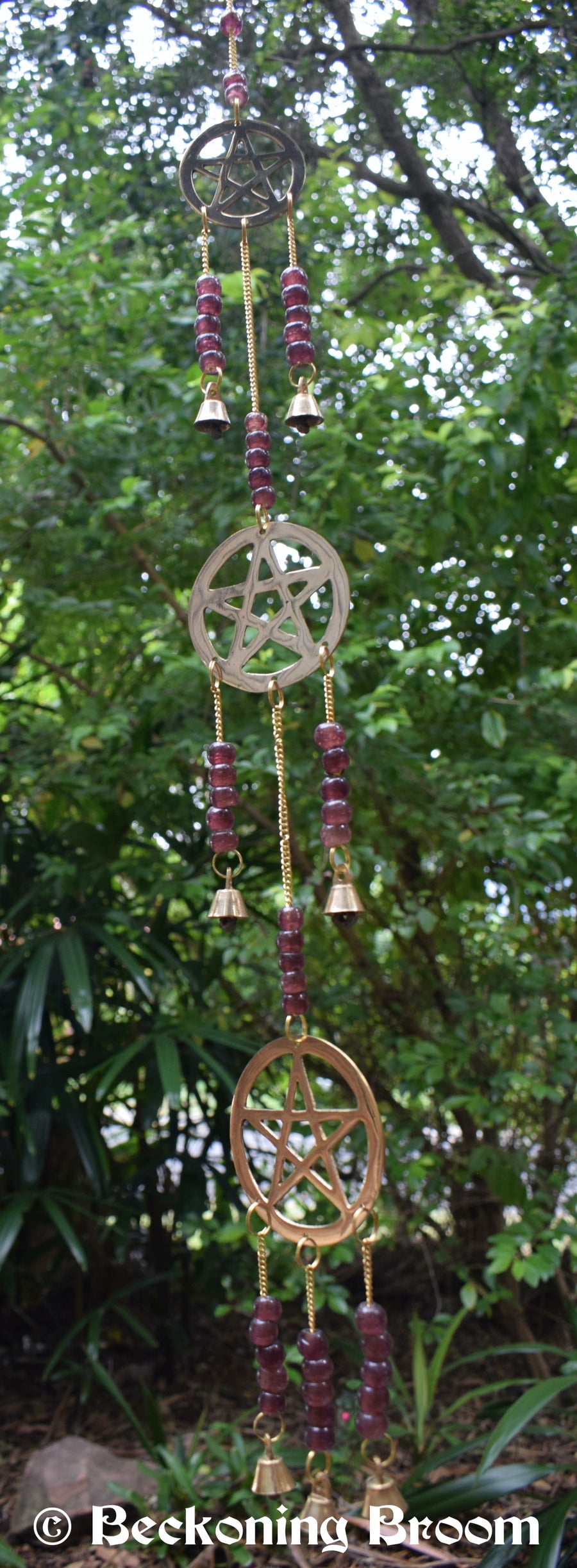 A long bronze metal wind chime with 3 pentagram pentacles, grape purple glass beads and bronze metal bells hangs in the garden.