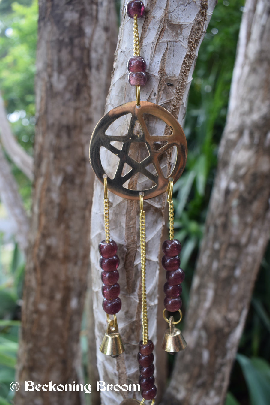 A long bronze metal wind chime hangs with pentagram pentacles, grape purple glass beads and bronze metal bells hangs in the garden.