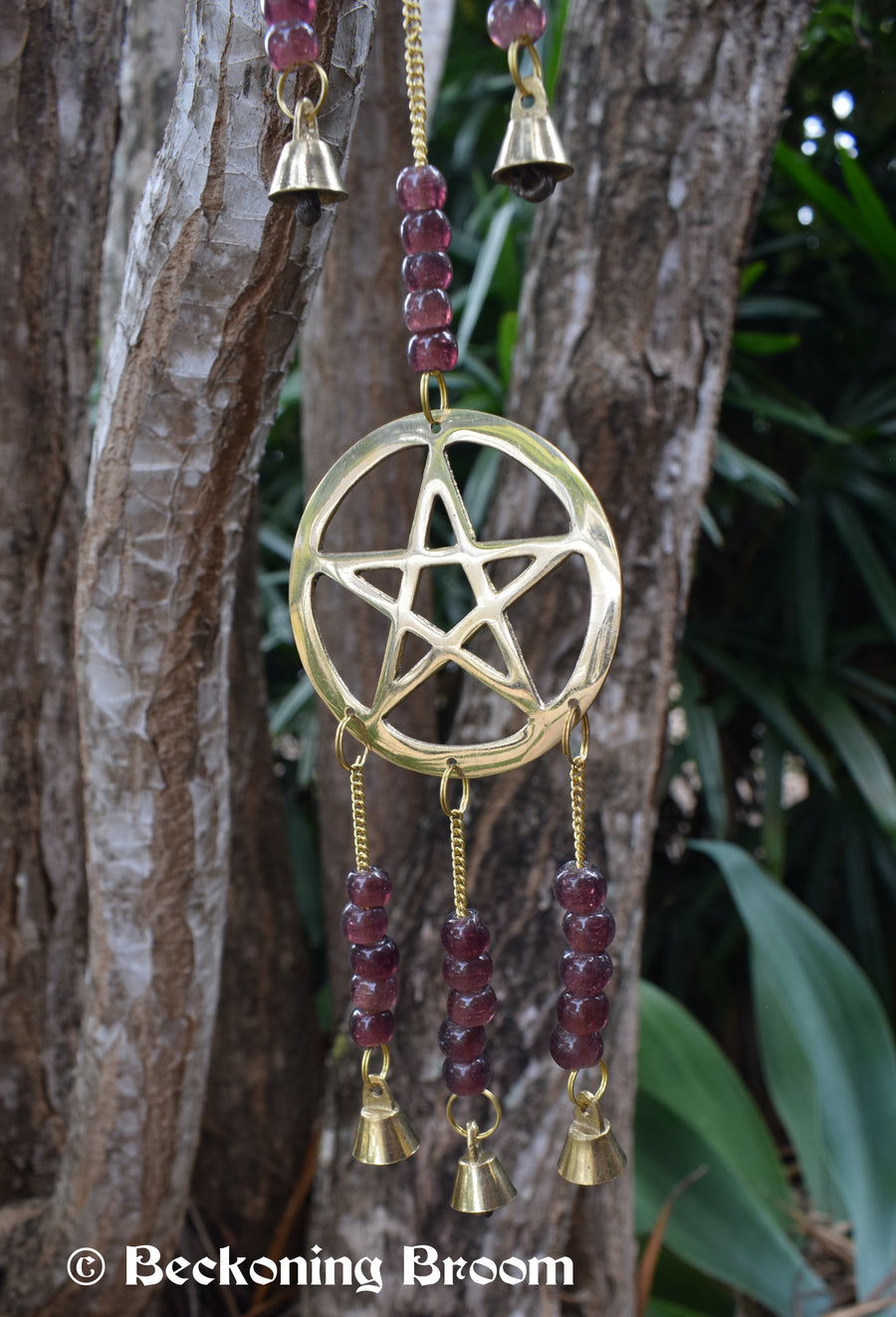 A long bronze metal wind chime with pentagram pentacles, grape purple glass beads and bronze metal bells hangs in the garden.