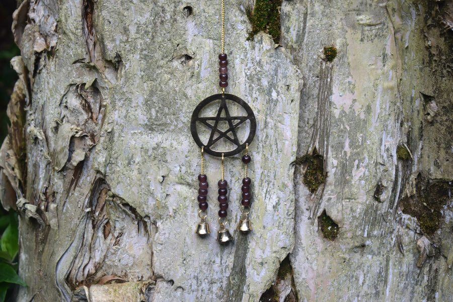 A grape-purple beaded bronze pentagram pentacle metal wind chime rests against a paperbark tree in the garden