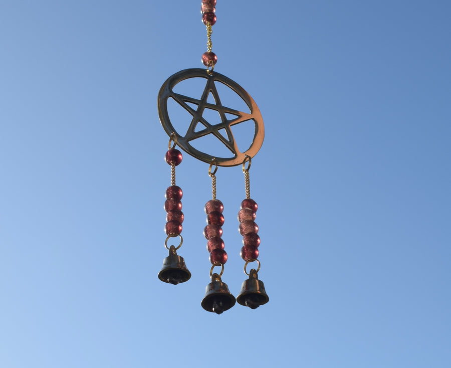 A grape-purple beaded bronze pentagram pentacle metal wind chime hangs in the garden with sunlight with blue sky in the background