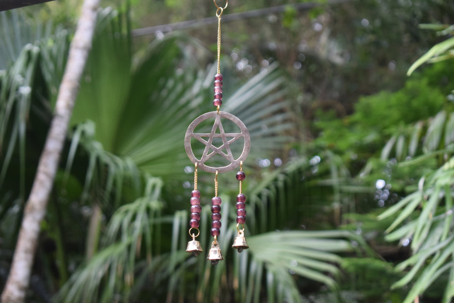 A grape-purple beaded bronze pentagram pentacle metal wind chime hangs in the garden