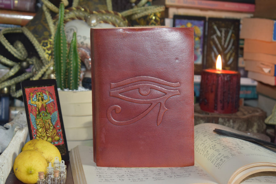 A leather-bound book of shadows with an eye of horus embossed on the cover sits on an altar