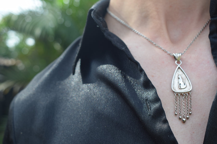 Neck of person wearing black shirt with sterling silver cat pendant with fringing on chain